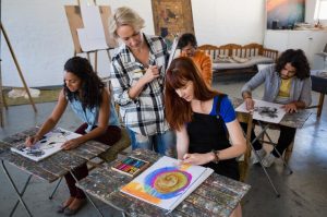 high-angle-view-teacher-examining-students-painting-table_107420-29317